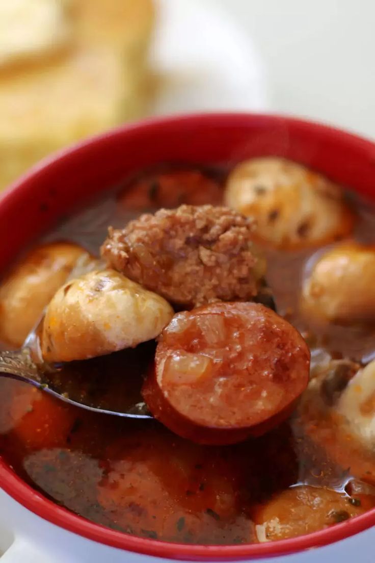 a red bowl filled with stew and meat on top of a white tablecloth next to bread