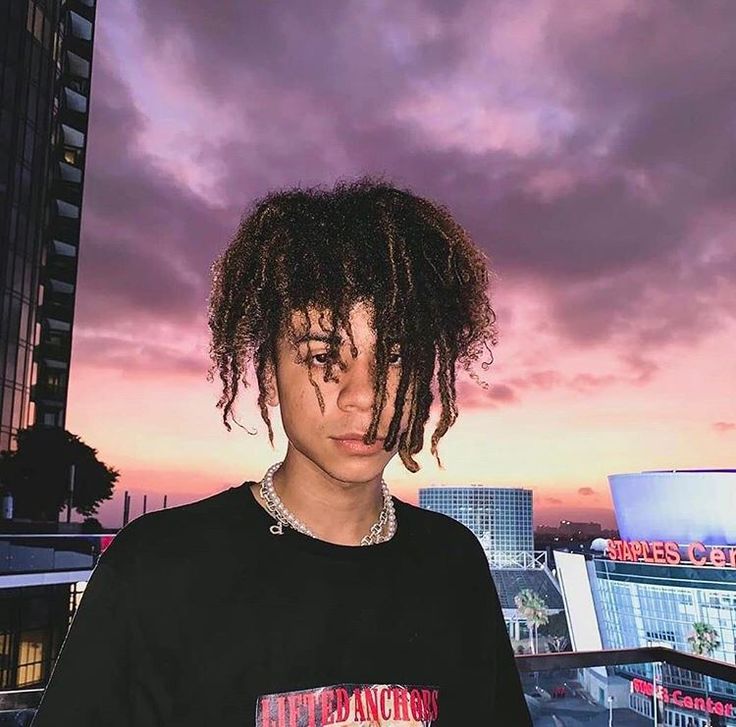 a young man with dreadlocks standing in front of a cityscape at sunset