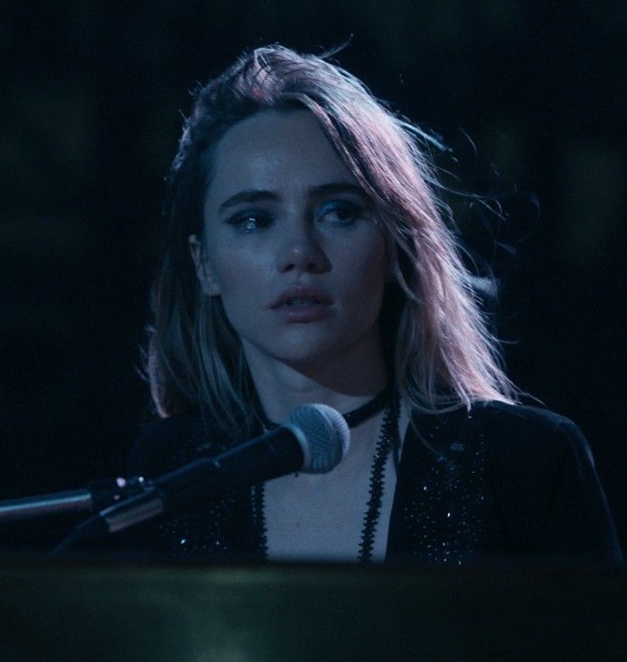 a woman standing next to a microphone in front of a keyboard on a dark stage