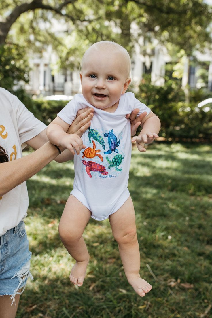 Bring all the color with our original sea turtle onesie! T-shirts & Onesies are a soft spun 100% polyester How are they printed? It's magic basically, but if you want the scientific answer... The process is called Dye Sublimation. Artwork is printed onto a sheet of high-release paper and transferred onto apparel using heat and pressure. Heat converts the solid dye particles into a gas — known as sublimation — and bonds them to the polyester fibers. Unlike screen printing, the dye is absorbed by Pre-shrunk Short Sleeve Onesie For Playtime, Casual Short Sleeve Onesie For Beach, Casual Short Sleeve Onesie For The Beach, Casual Short Sleeve Beach Onesie, Playful White Stretch Onesie, White Stretch Playful Onesie, Playful Printed Short Sleeve Bodysuit, Turtle Onesie, Turtle Homes