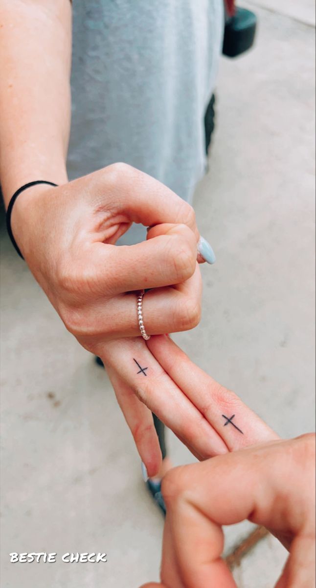 two people holding hands with cross tattoos on their fingers