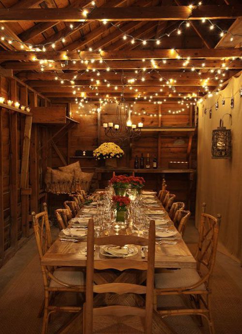 a dining room with lights strung from the ceiling and wooden tables set up for dinner