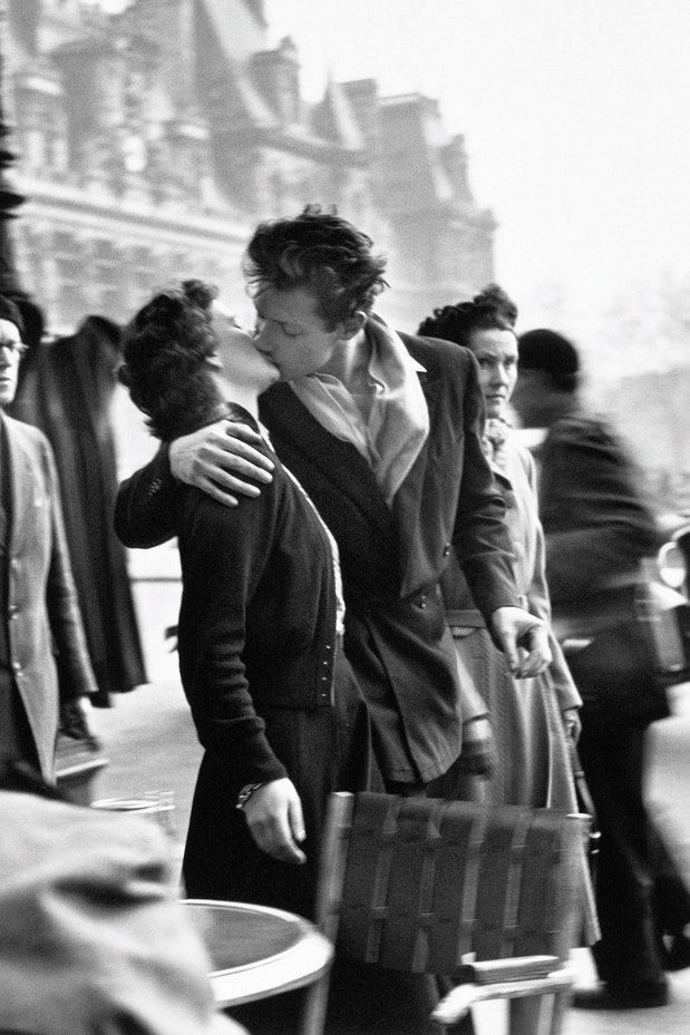 black and white photograph of two women embracing each other on the street with people in the background