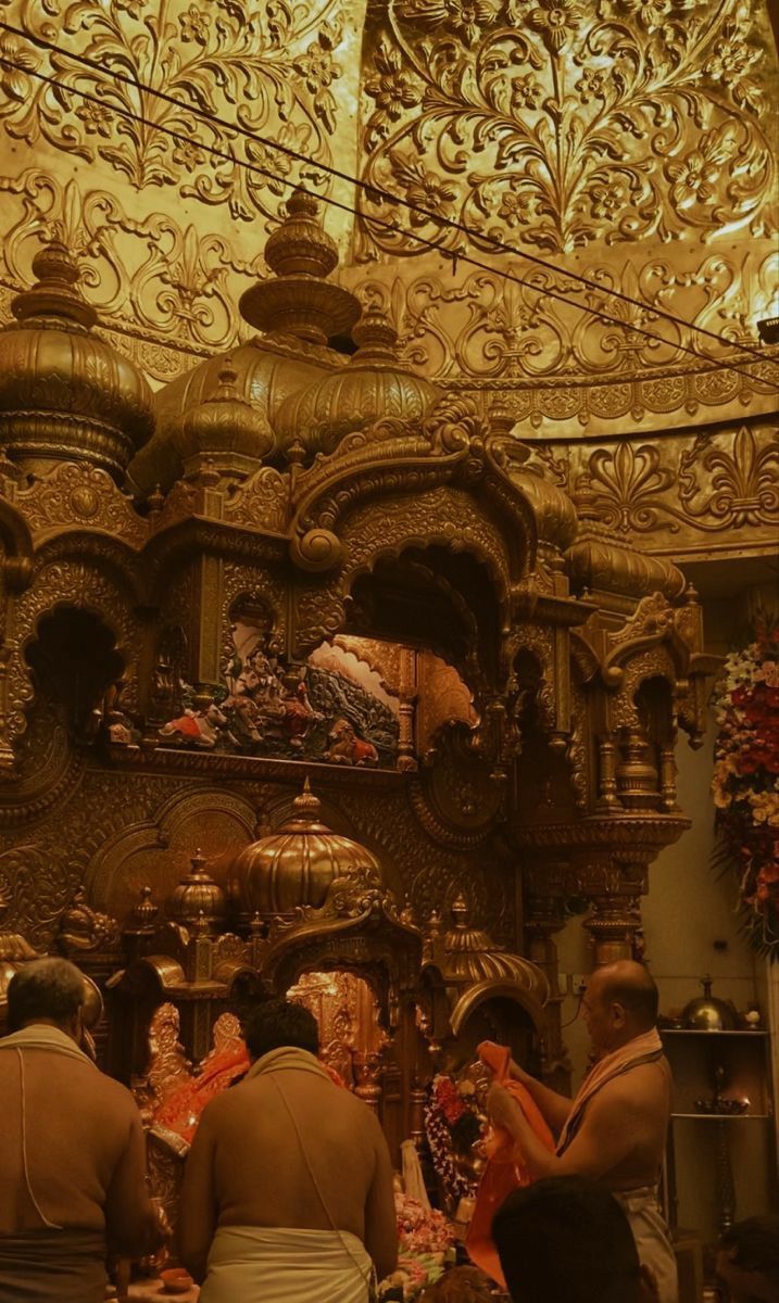 some people are standing in front of a gold colored shrine with carvings on the walls