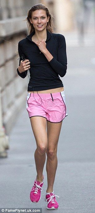 a woman in pink shorts and black shirt walking down the street with her hand on her hip