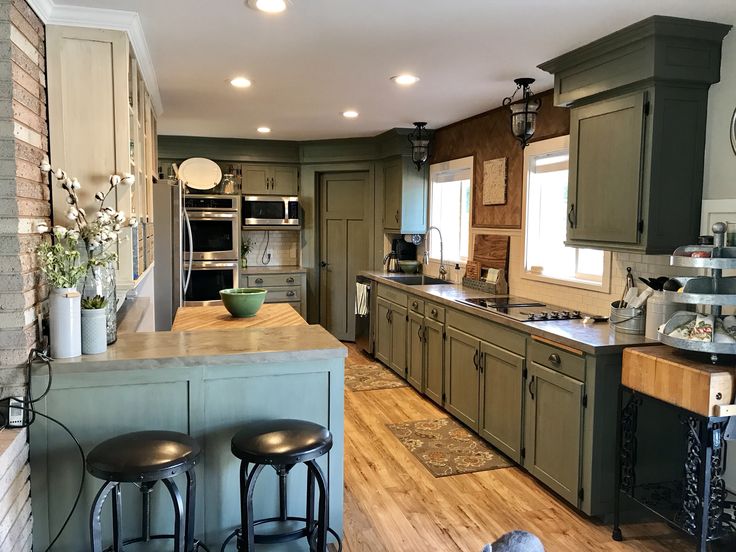 a kitchen with green cabinets and stools next to an island in front of a stove top oven