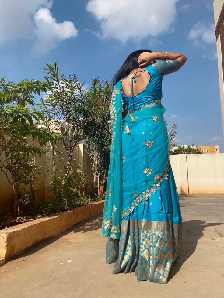 a woman in a blue sari is standing on the sidewalk with her arms behind her head