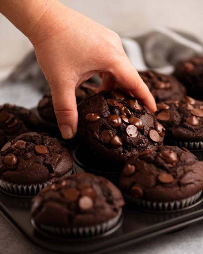 a person picking up a chocolate muffin from a tray