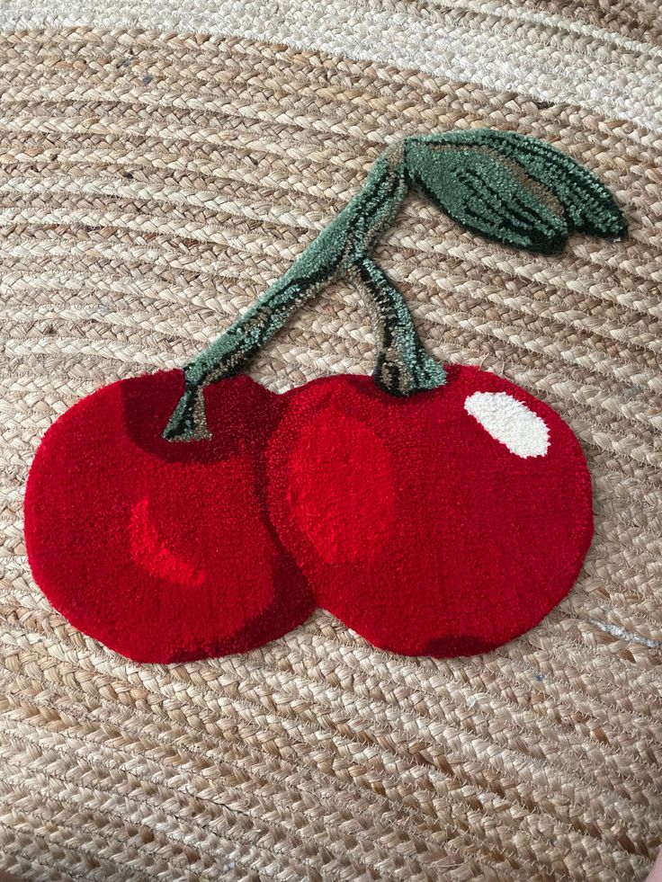 two red cherries with green leaves on top of a piece of knitted material