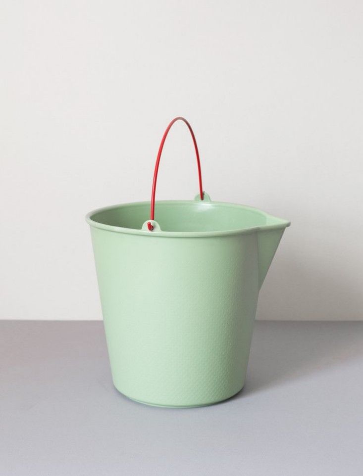 a green bucket with a red handle on the top is sitting on a gray surface