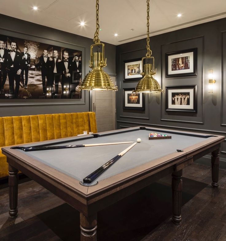 a pool table in a room with pictures on the wall and lights hanging above it