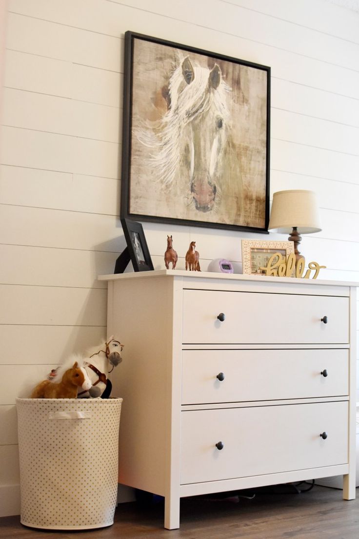 a white dresser sitting next to a painting on the wall