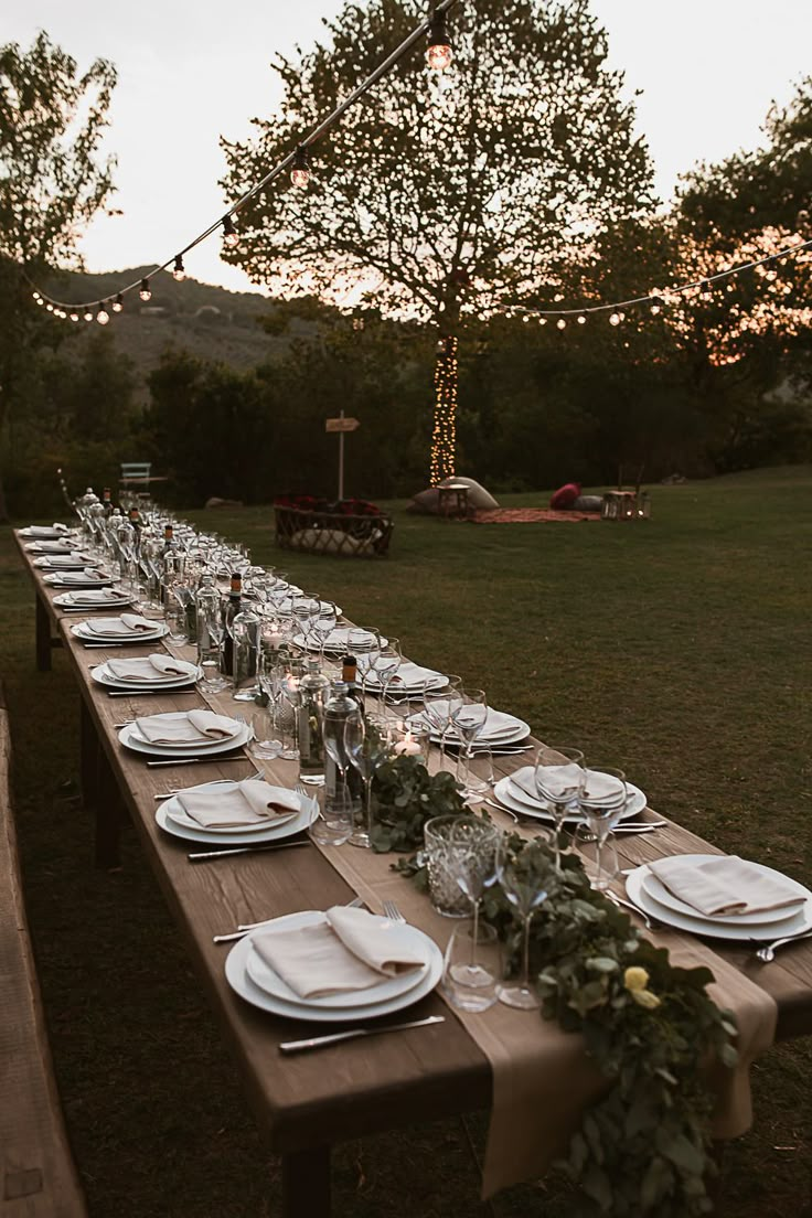 a long table with plates and silverware on it in the middle of a field