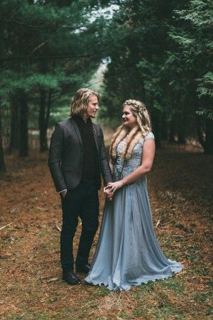 a man and woman standing next to each other in front of trees with long hair