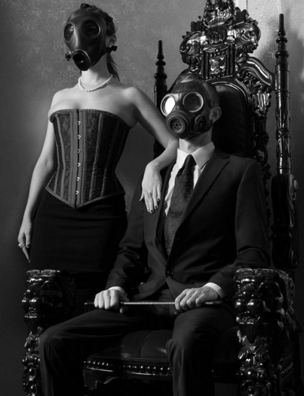 a man in a gas mask sitting next to a woman wearing a dress on a chair