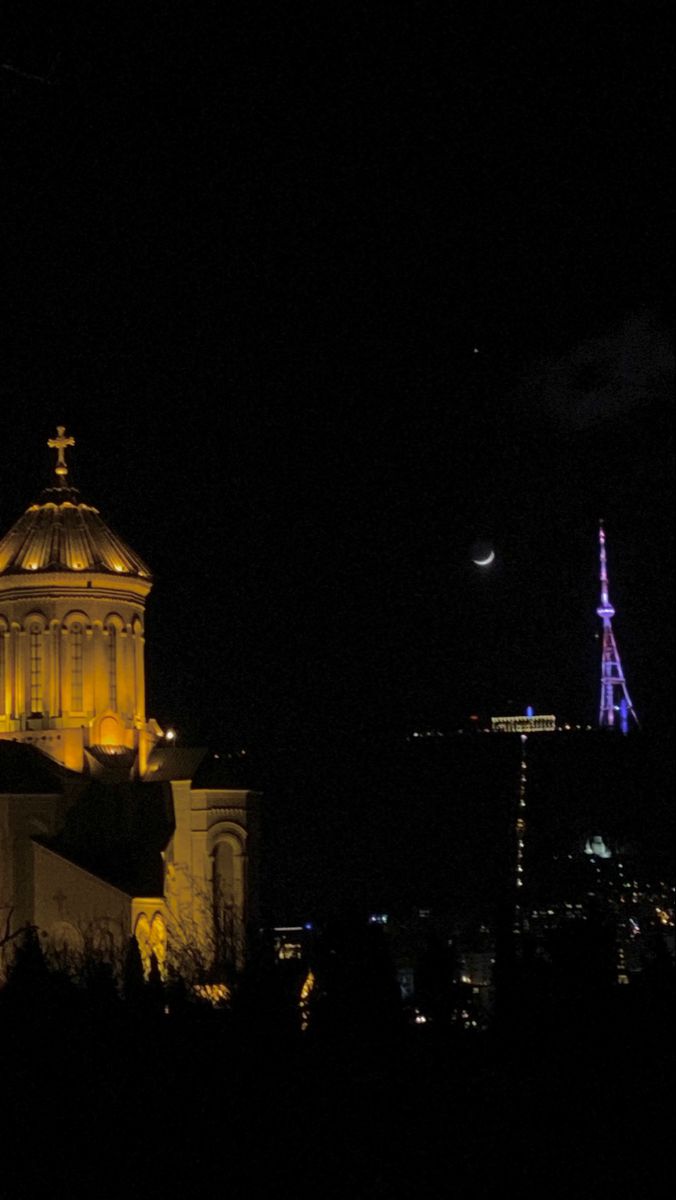 the building is lit up at night with lights on it's roof and spire