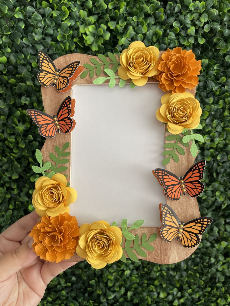 a person holding up a wooden frame with flowers and butterflies on it