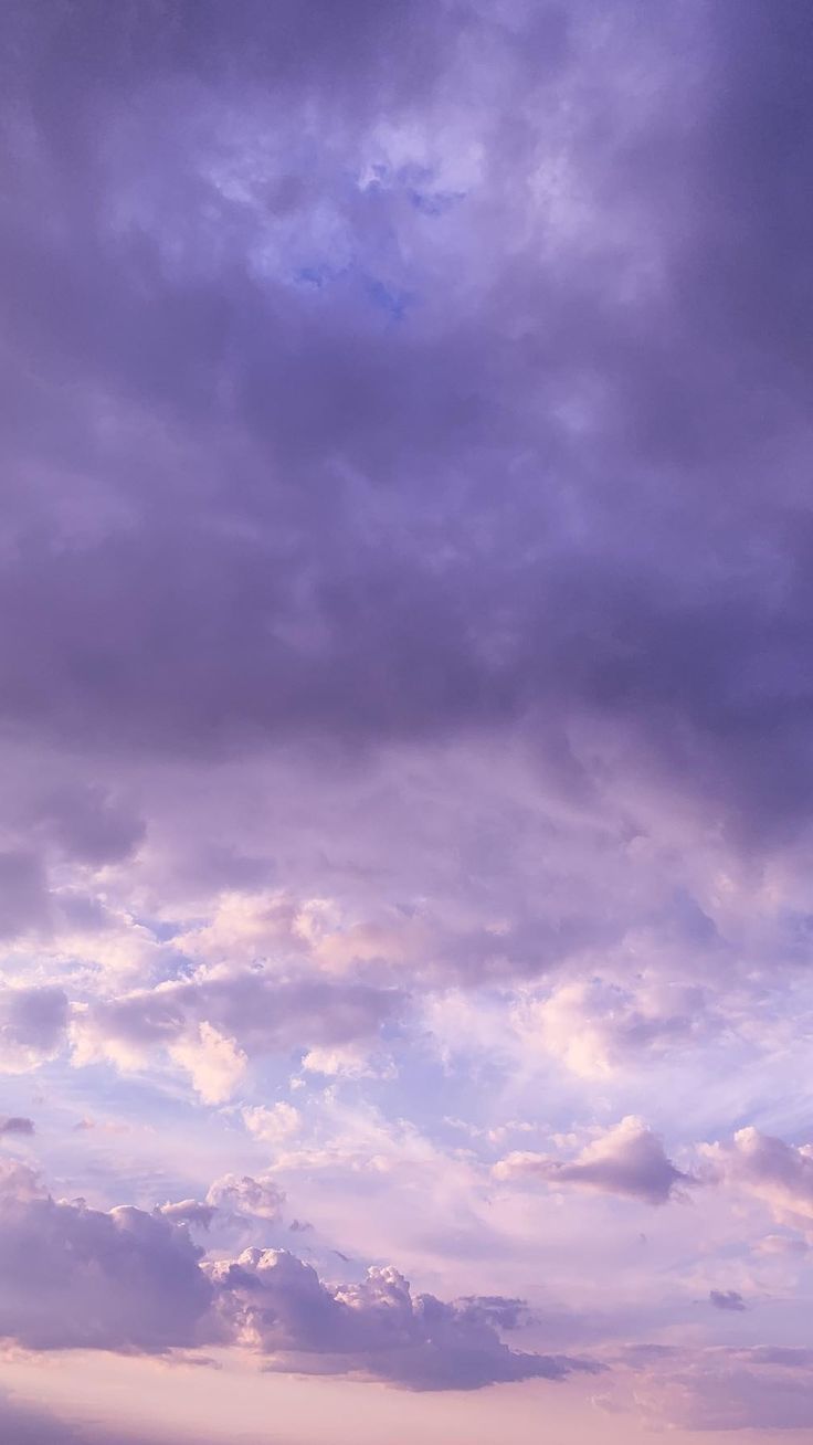 two people standing on the beach with their surfboards under a cloudy blue and purple sky