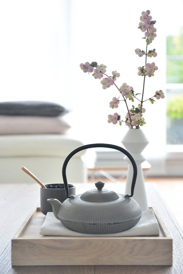 a tea kettle and cup on a tray with flowers in the vase next to it