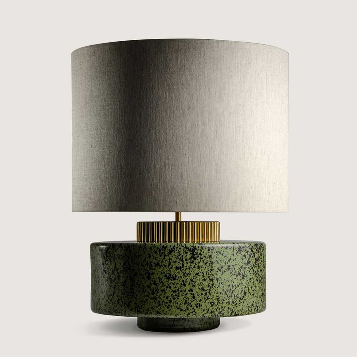 a green table lamp with a grey shade on top and a gold trim around the base