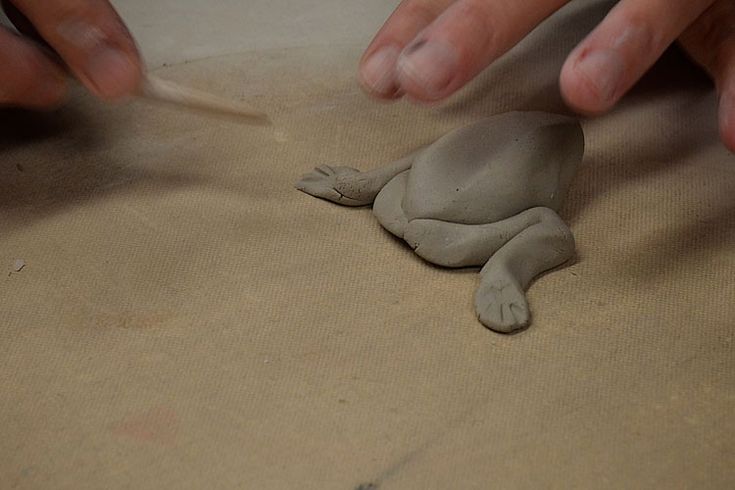 someone is making a clay turtle out of clay with their hands on the ground and another hand reaching for it