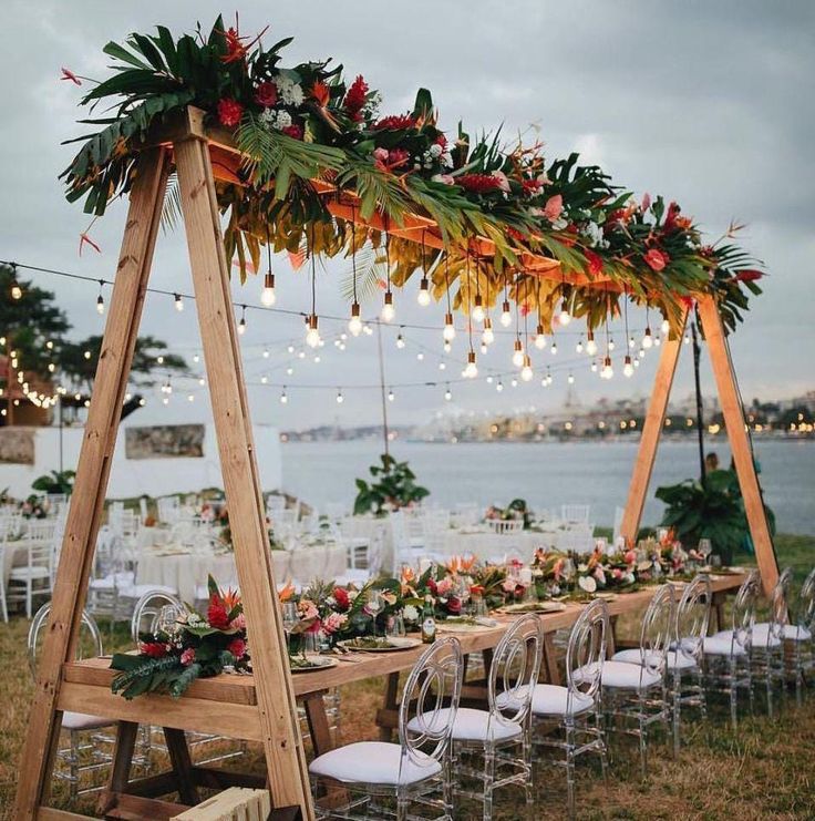 a wooden table topped with lots of flowers and greenery next to an outdoor dining area