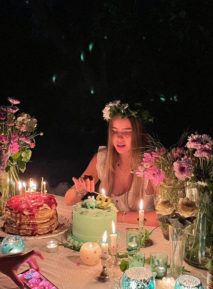 a woman sitting at a table in front of a cake with lit candles on it