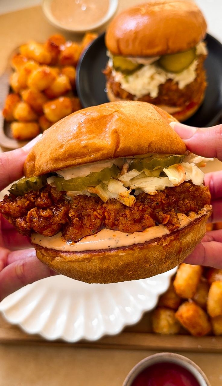 a person holding a sandwich in front of some other food on a plate with sauce and ketchup