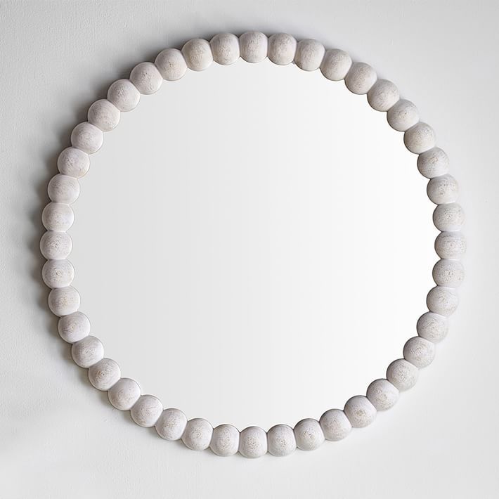 a white beaded necklace hangs on the wall next to a round mirror that is hanging above it