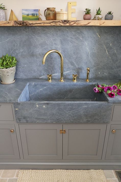 a kitchen sink sitting under a window next to a shelf with potted plants on it