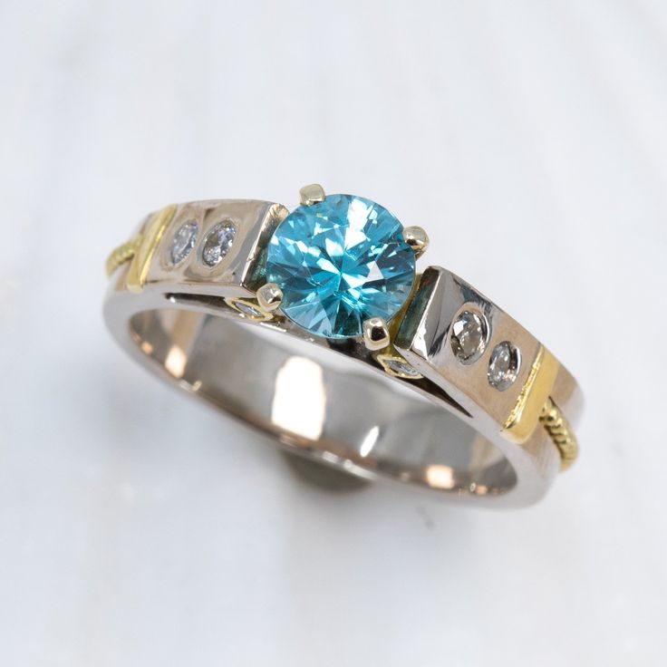 This breathtaking Blue Zircon & Diamond Classical Ring presents the perfect blend of classic and modern elements. Crafted from 18K palladium white gold, the ring sparkles with a dazzling 1.05ct blue zircon and is subtly accented with 18KY gold granulation and diamonds for a truly eye-catching display. Truly exquisite, this timeless piece is sure to turn heads. 18K palladium white gold ring with 18K yellow gold granulation is set with a gorgeous 1.05ct blue zircon and .20cttw VS/G-H diamonds. Siz Luxury Light Blue Ring With Brilliant Cut, Luxury Light Blue Brilliant Cut Ring, Light Blue Diamond Ring With Brilliant Cut, Blue Moissanite Diamond Ring With Brilliant Cut, Luxury Blue Ring With Tension Setting, Classic Blue Topaz Ring With Tension Setting, Blue Topaz Ring With Diamond Accents In Platinum, Blue Ring With Tension Setting For Wedding, White Gold Diamond Ring With Brilliant Cut Blue Topaz