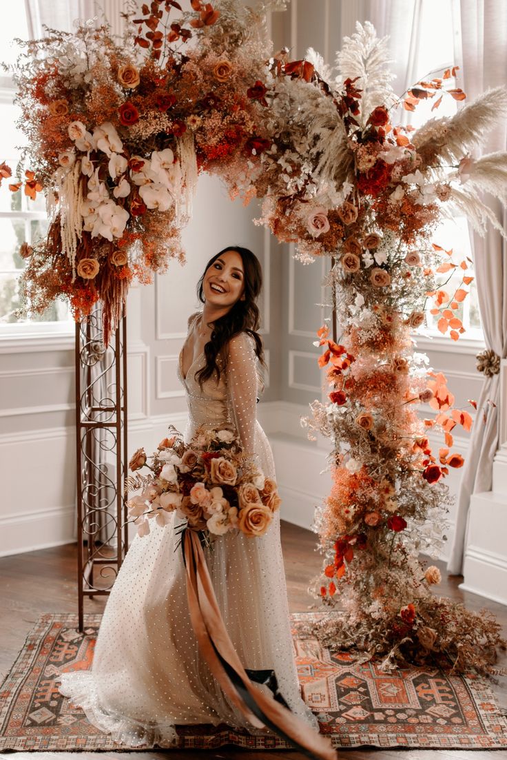 a woman in a wedding dress is standing under an arch with flowers and feathers on it