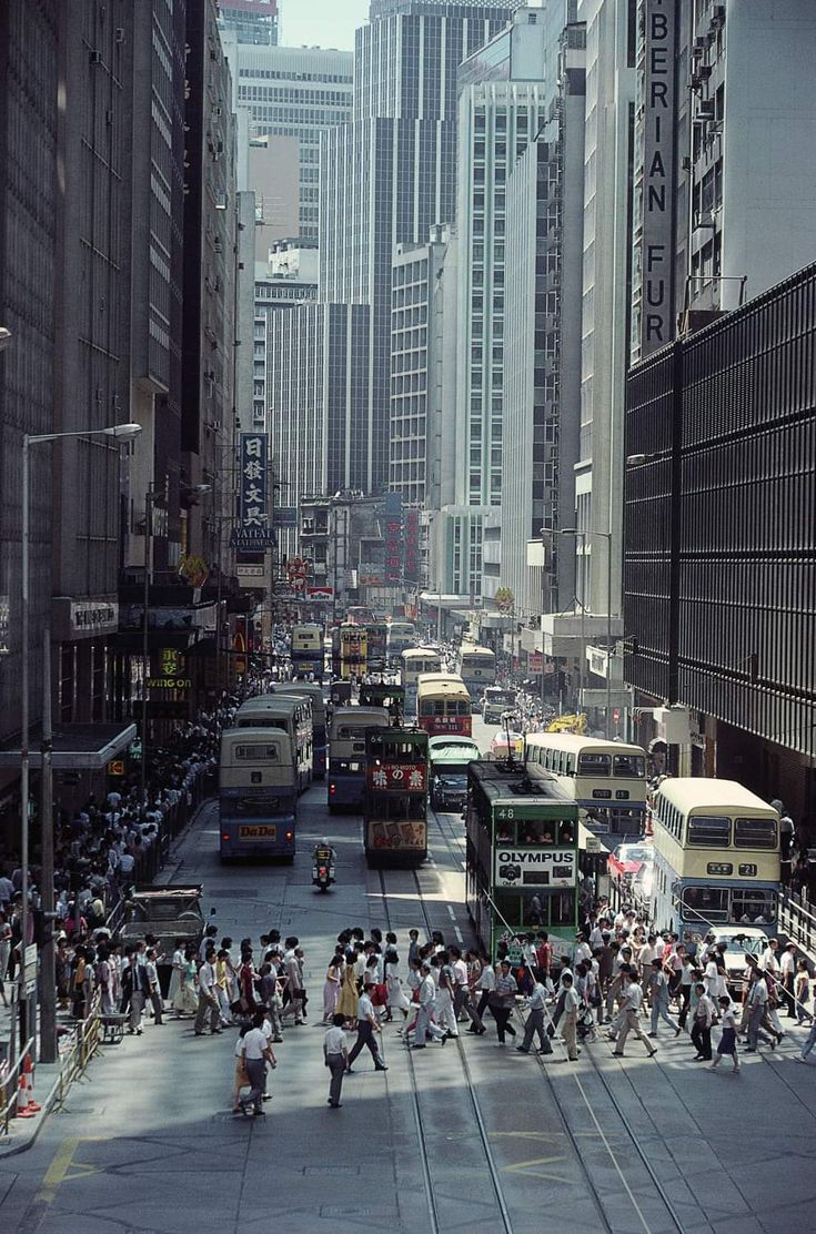 a busy city street filled with lots of buses and people walking on the side of it