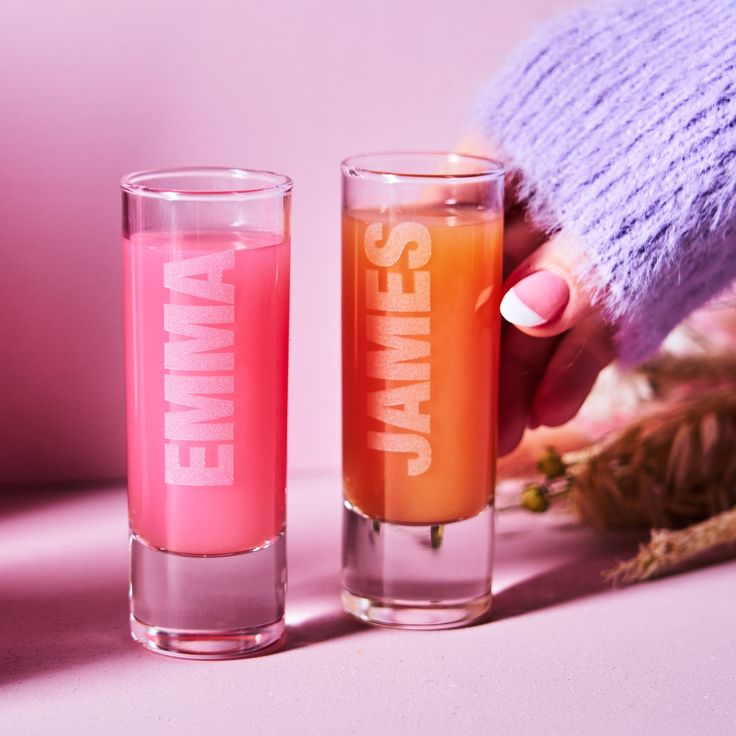 two shot glasses with pink and orange liquid next to each other