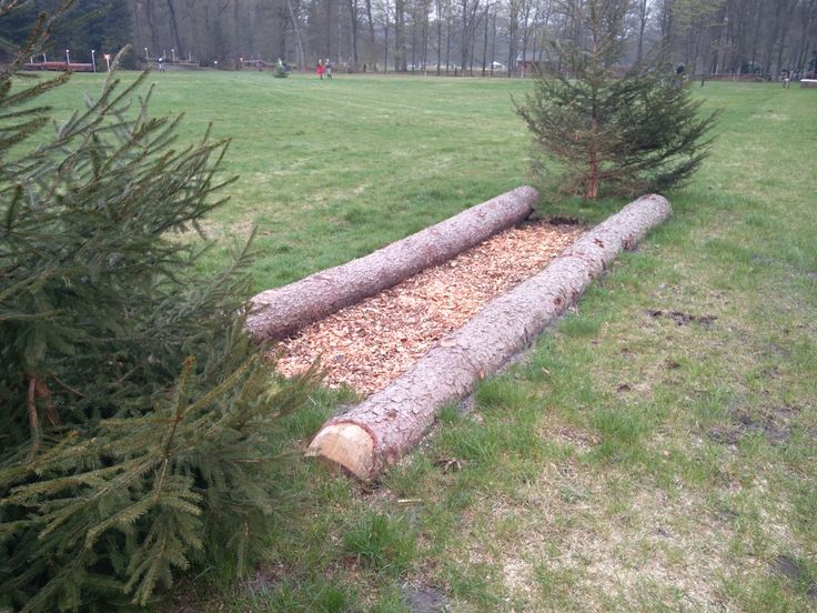 a large log sitting in the middle of a grass field next to a pine tree