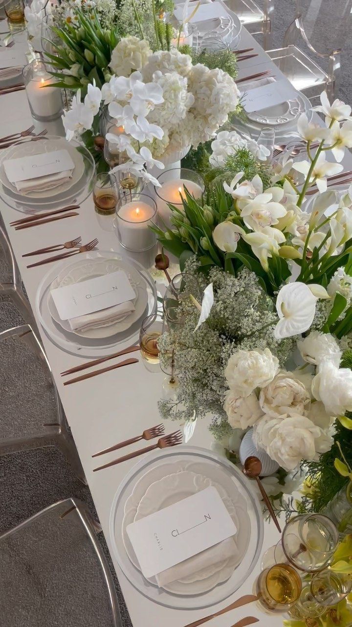 a long table is set with white flowers and place settings for the guests to sit at