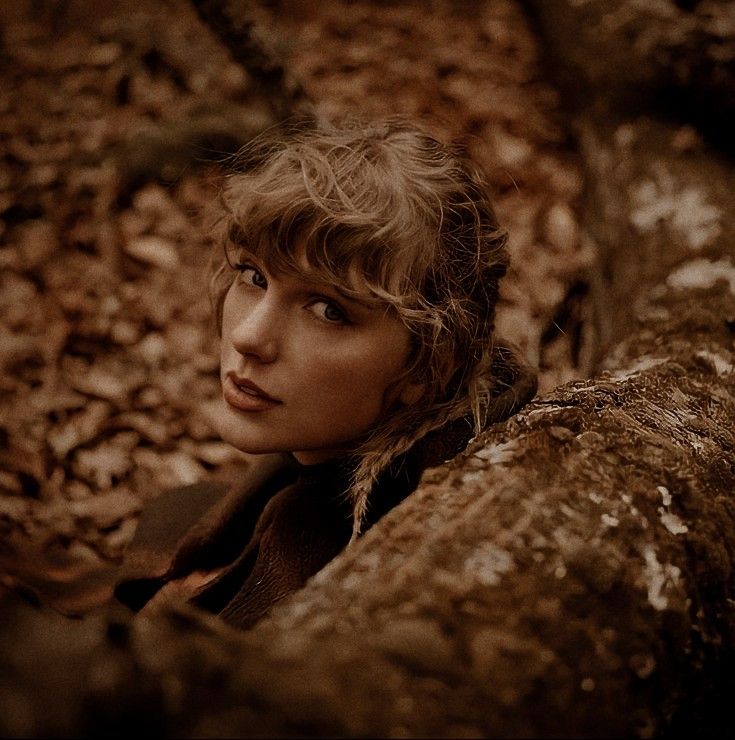 a woman with blonde hair is leaning against a tree trunk and looking up at the camera