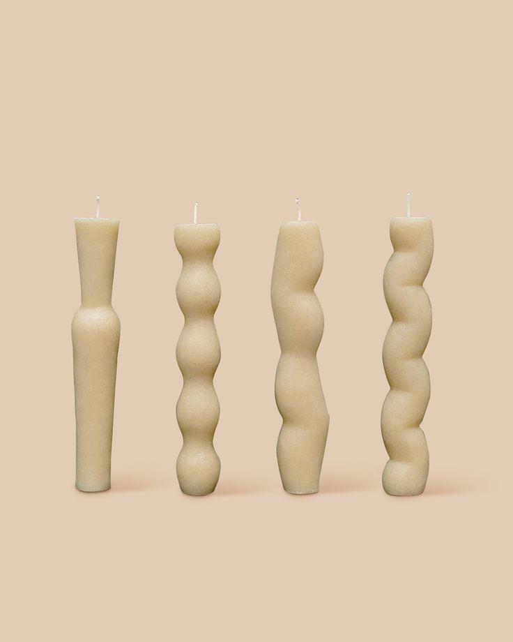 three candles are lined up next to each other in different shapes and sizes on a beige background