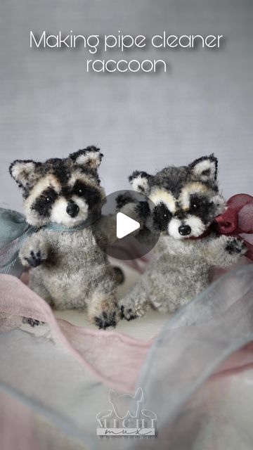 two stuffed raccoons sitting next to each other on top of a cloth covered blanket