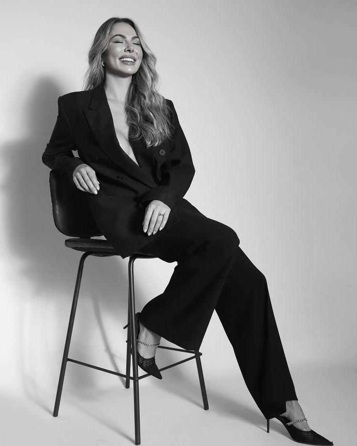 a woman sitting on top of a chair in a black suit and high heeled shoes