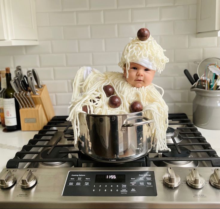 a baby in a chef's hat sitting on top of a stove next to a pot