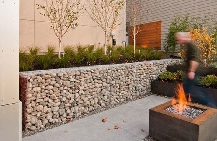 a man standing next to a fire pit in front of a building with trees and bushes