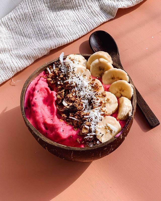 a bowl filled with yogurt and bananas on top of a pink surface next to a spoon