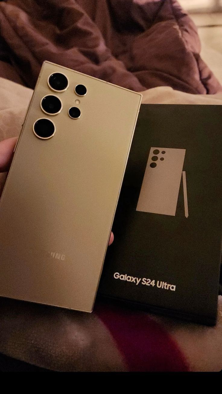 a person holding a gold cell phone next to an open box with the back side of it