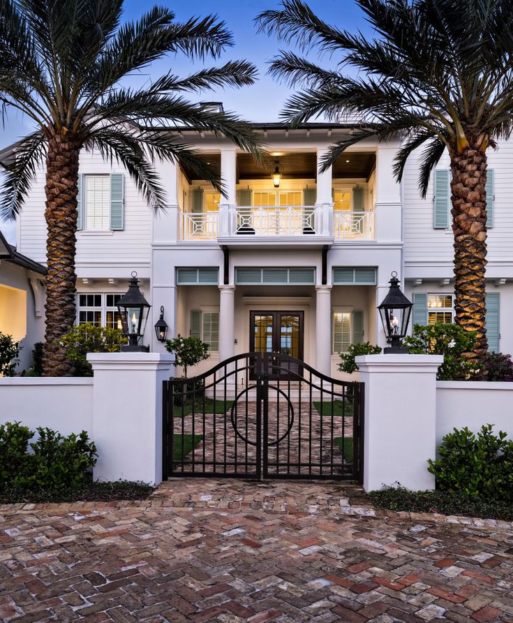 a large white house with palm trees in the front yard and gated entry way