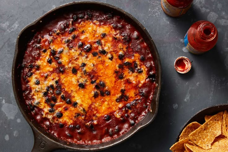 a skillet filled with chili and cheese next to tortilla chips on a table