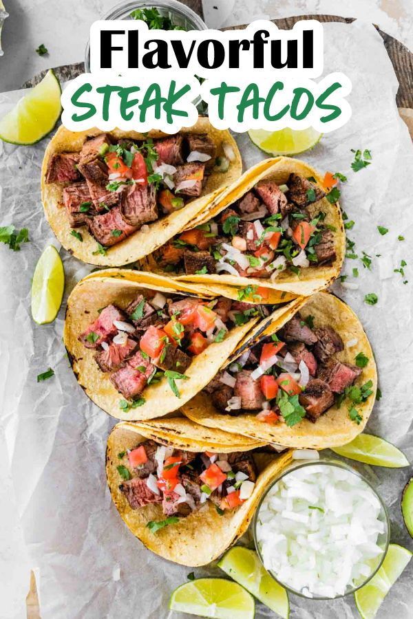 steak tacos with salsa and sour cream on the side, topped with lime wedges