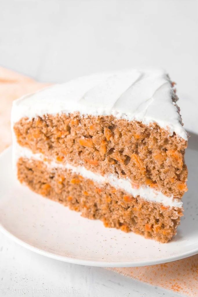 a slice of carrot cake with white frosting on a plate next to a fork