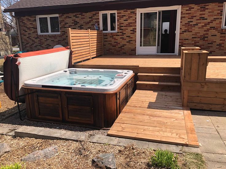 a hot tub sitting on top of a wooden deck next to a brick building and steps