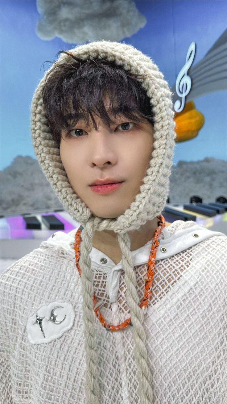 a young man wearing a knitted hoodie with an orange bead around his neck